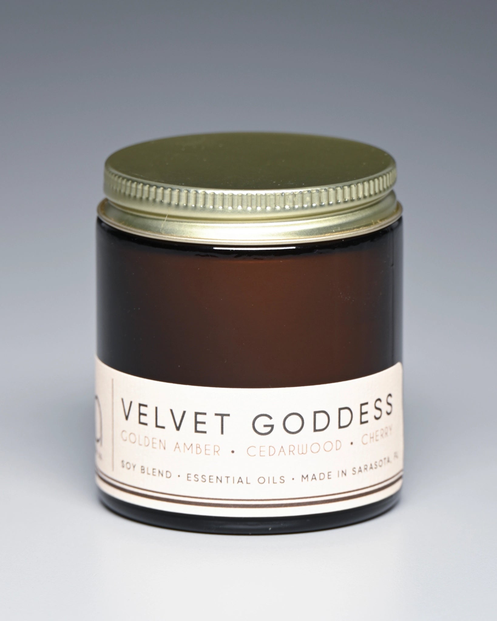 Jar of 'Velvet Goddess' candle with a gold lid on a gray background