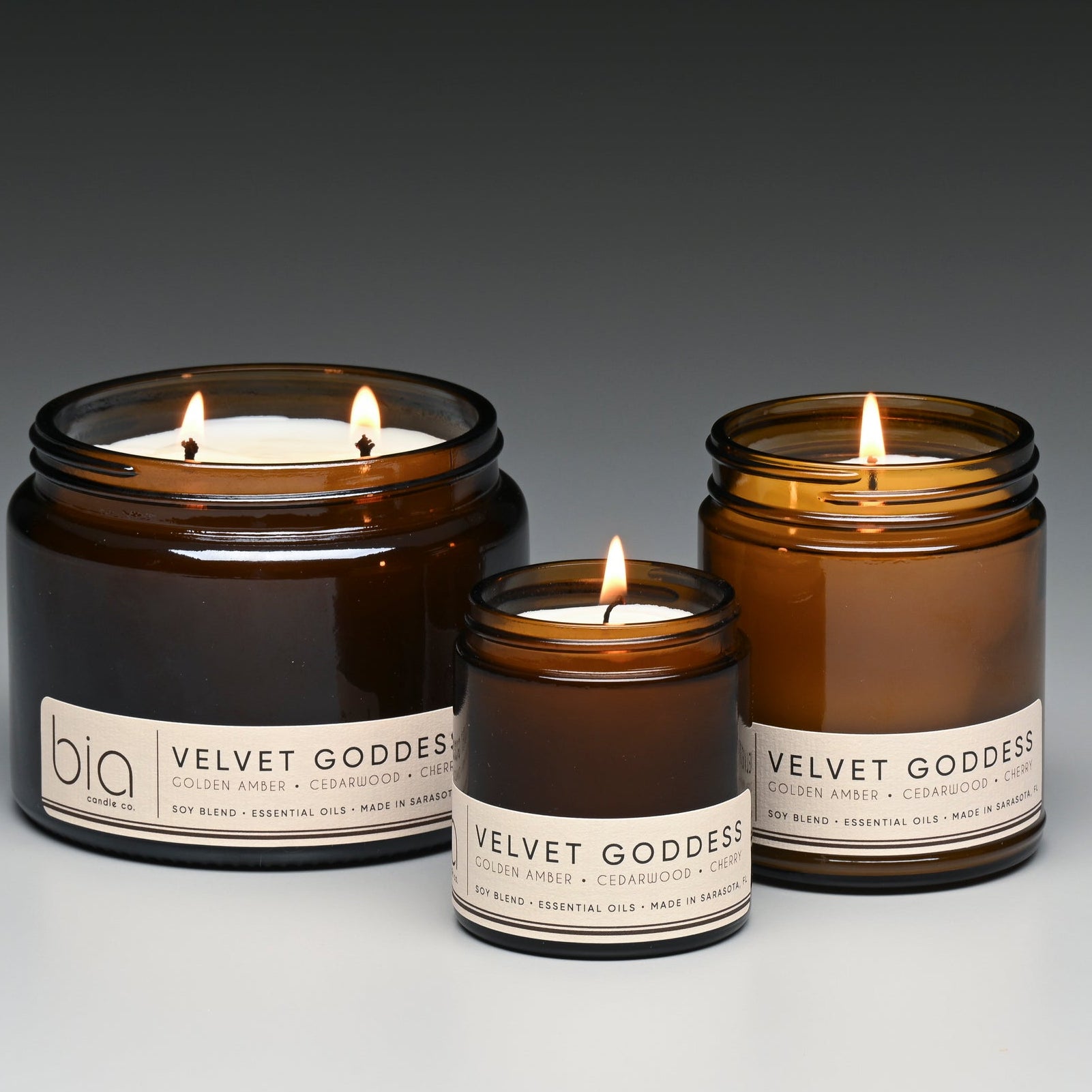 Three 'Velvet Goddess' candles in amber jars with visible flames on a gradient background.
