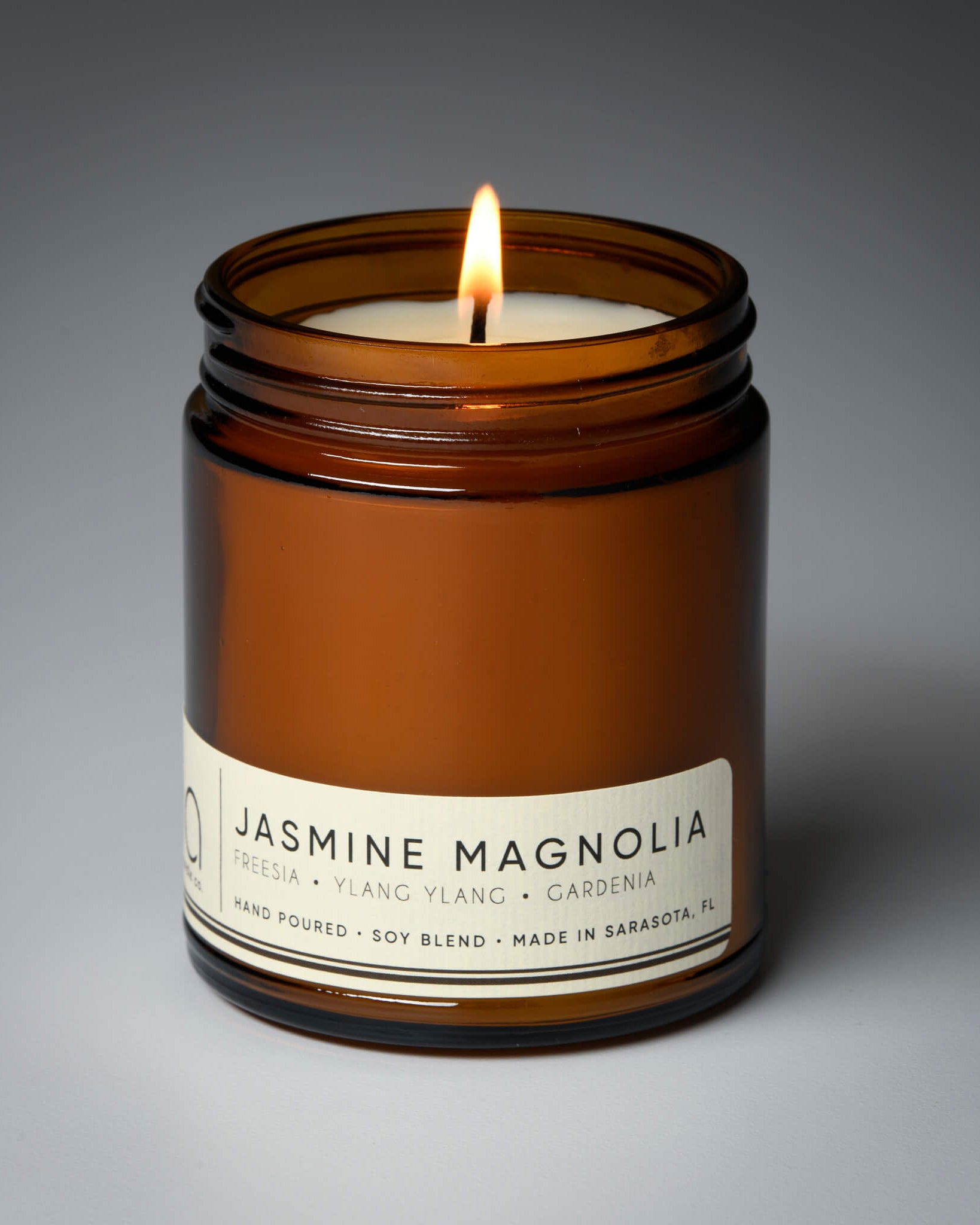 jasmine magnolia classic candle on gray backgroun with wick lit