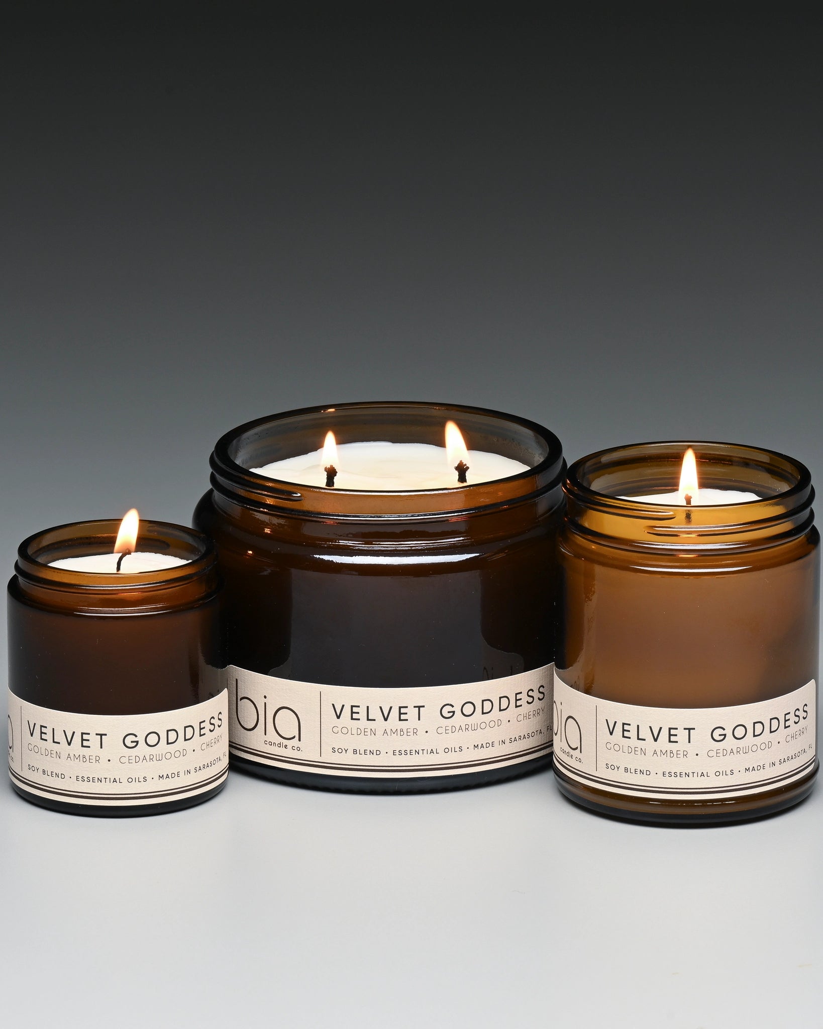 Three lit candles in brown jars with labels on a gray background