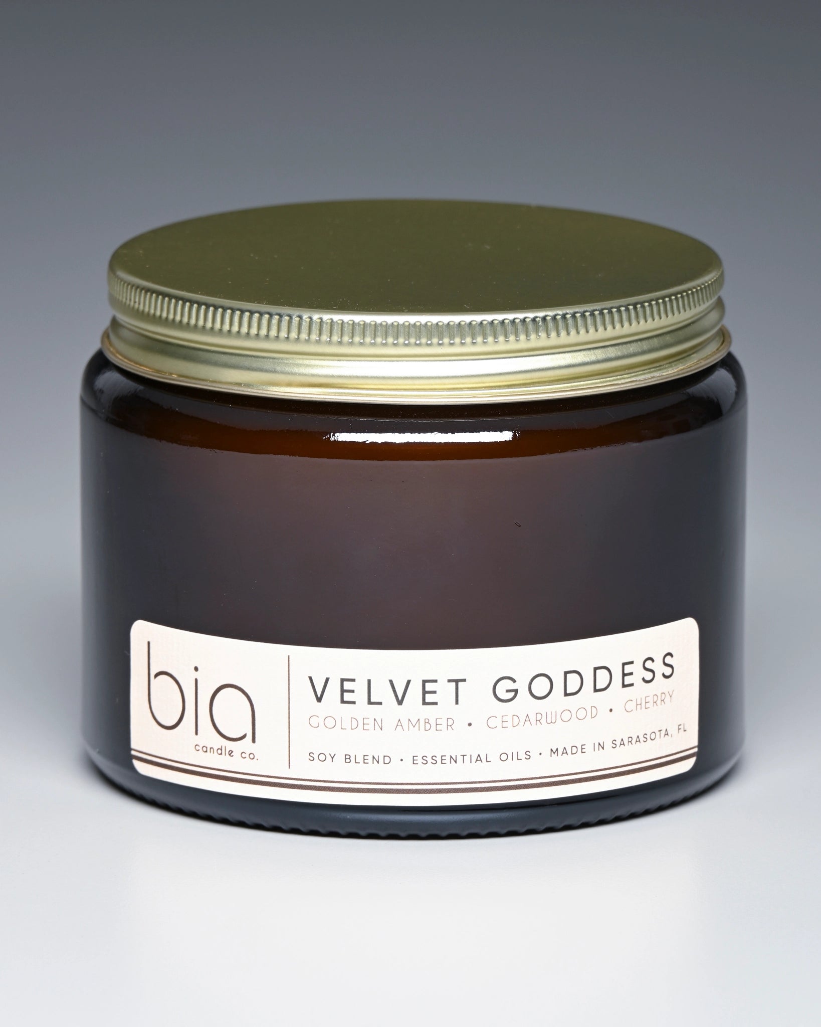 Jar of 'Velvet Goddess' candle by bia with a gold lid on a gradient background