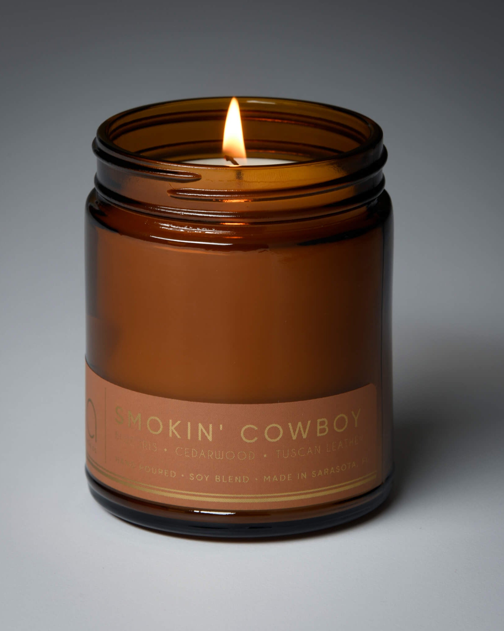lit single wick smokin cowboy soy candle on grey background