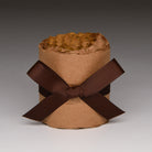 A brown kraft paper cylindrical container filled with crinkled brown tissue paper, tied with a wide dark brown ribbon bow in a studio setting.