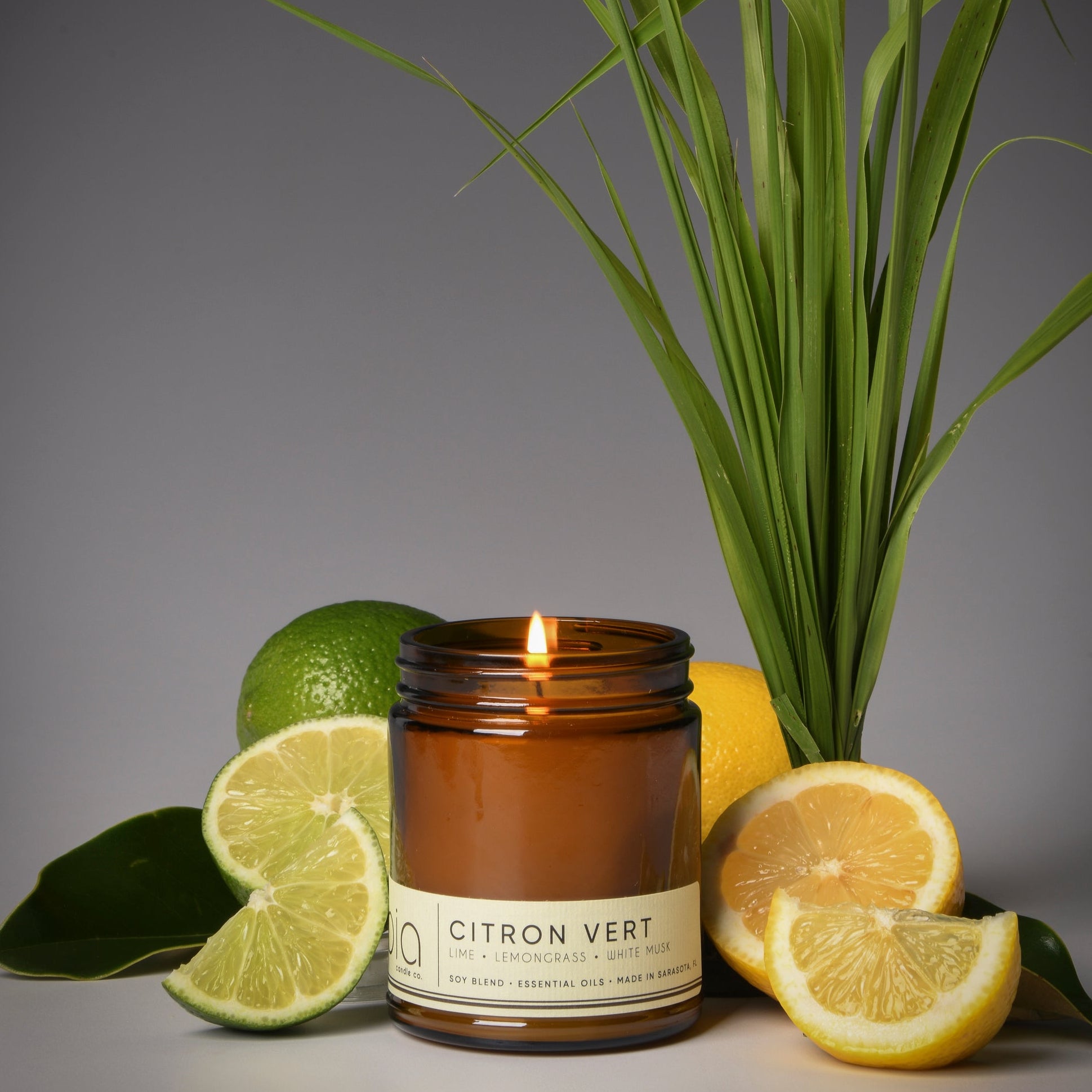 A brown BIA candle with a label reading 'Citron Vert' placed on a surface with green grass and lemon slices around it.