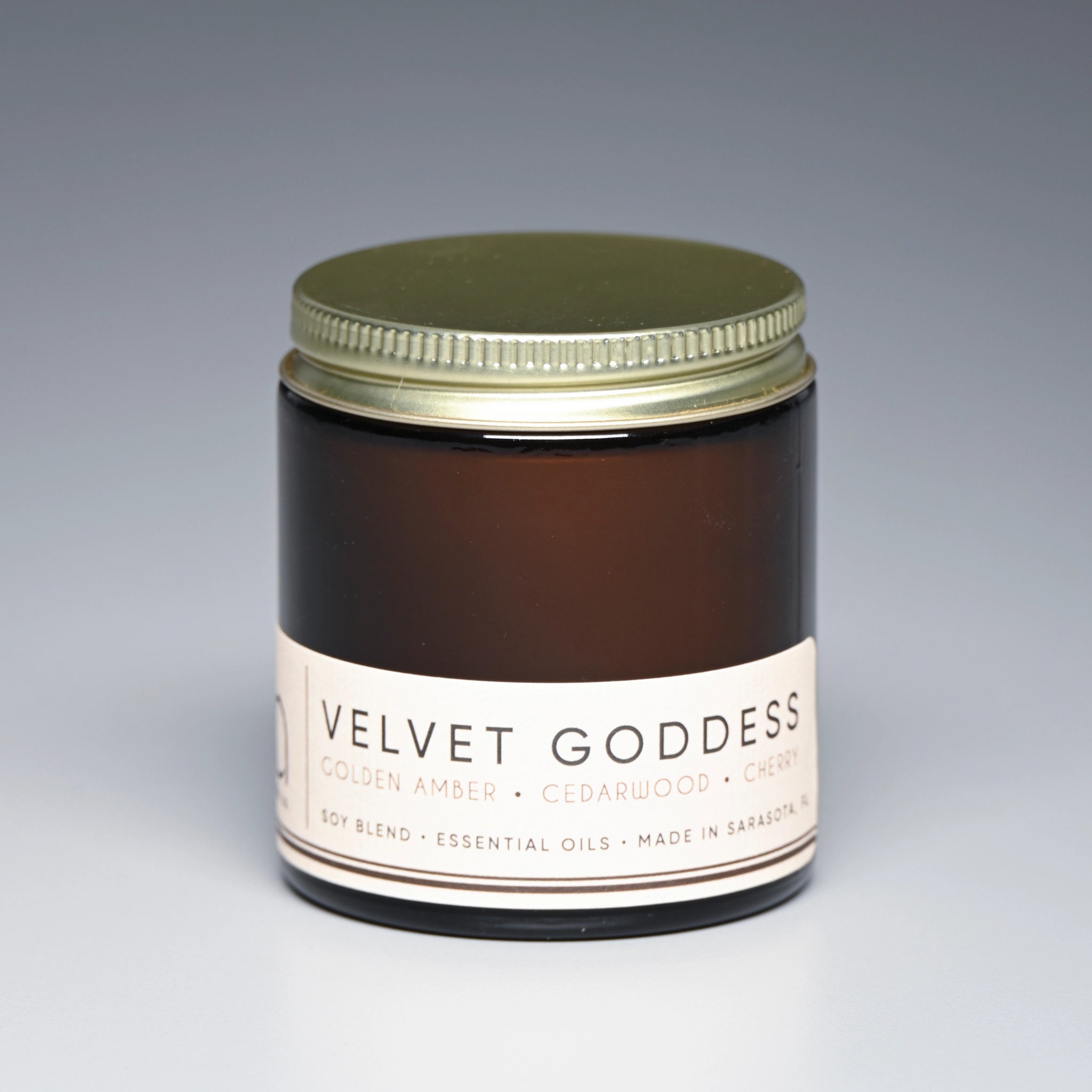 Jar of 'Velvet Goddess' candle with a gold lid on a gray background