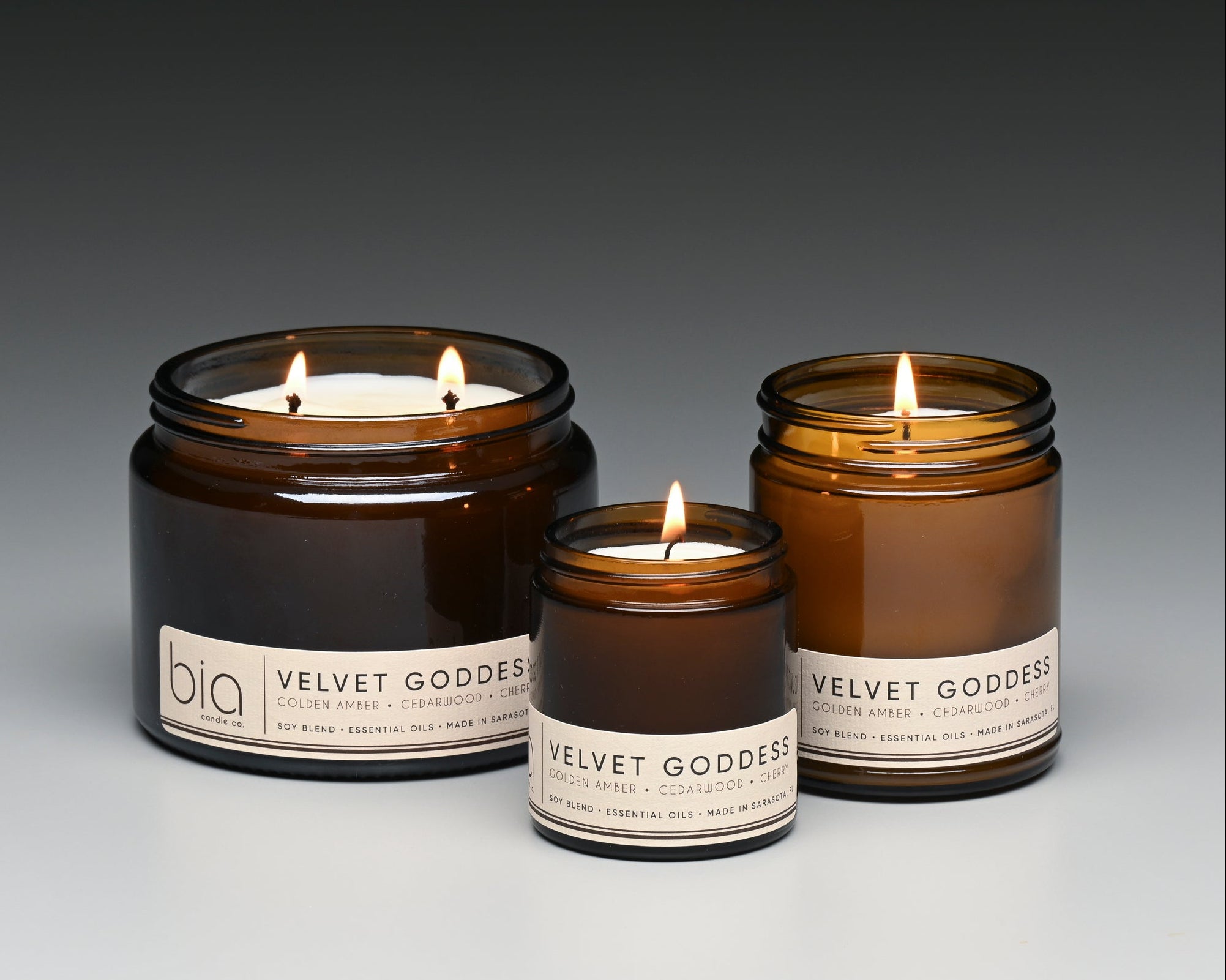 Three 'Velvet Goddess' candles in amber jars with visible flames on a gradient background.