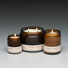 Three lit candles in brown jars with labels on a gray background