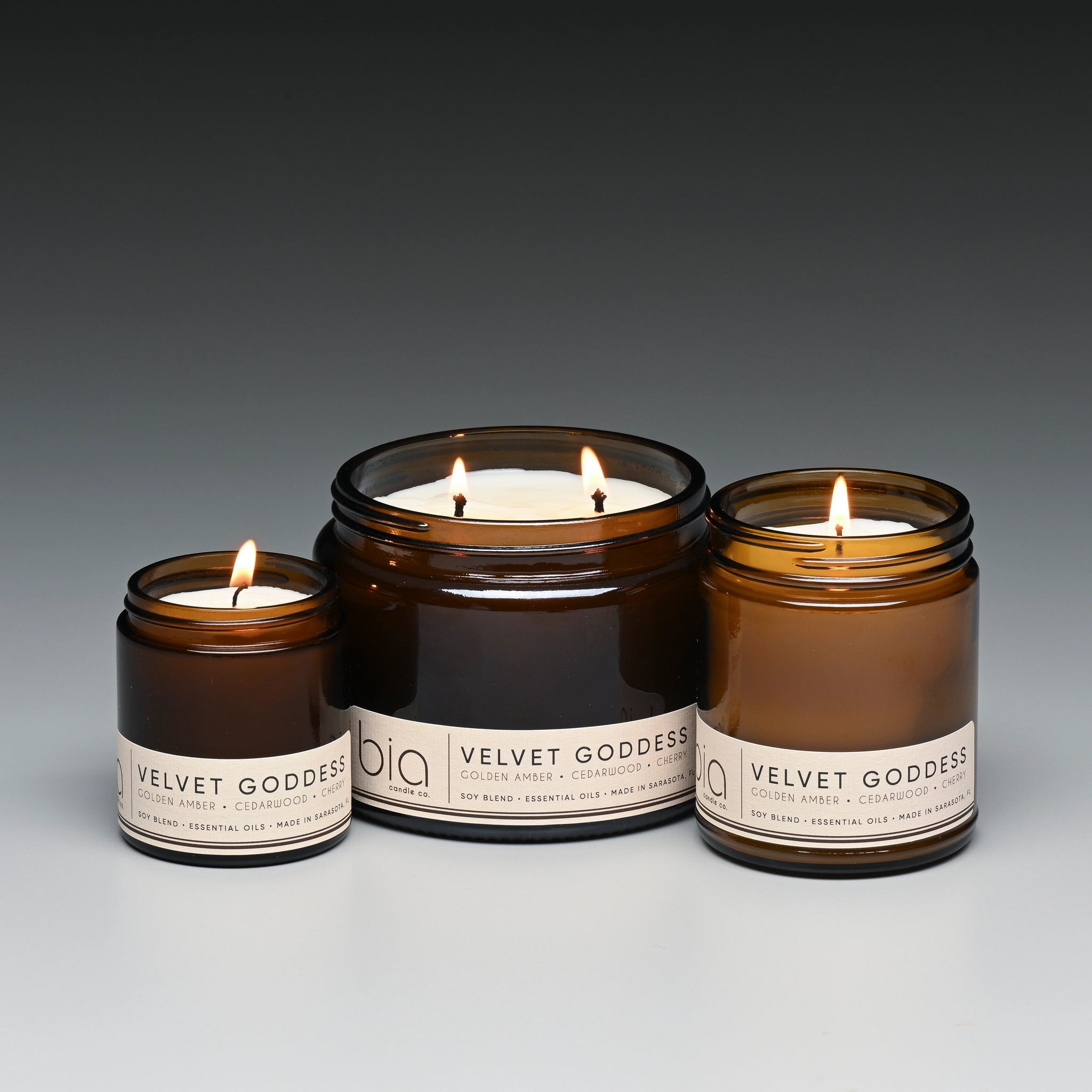 Three lit candles in brown jars with labels on a gray background