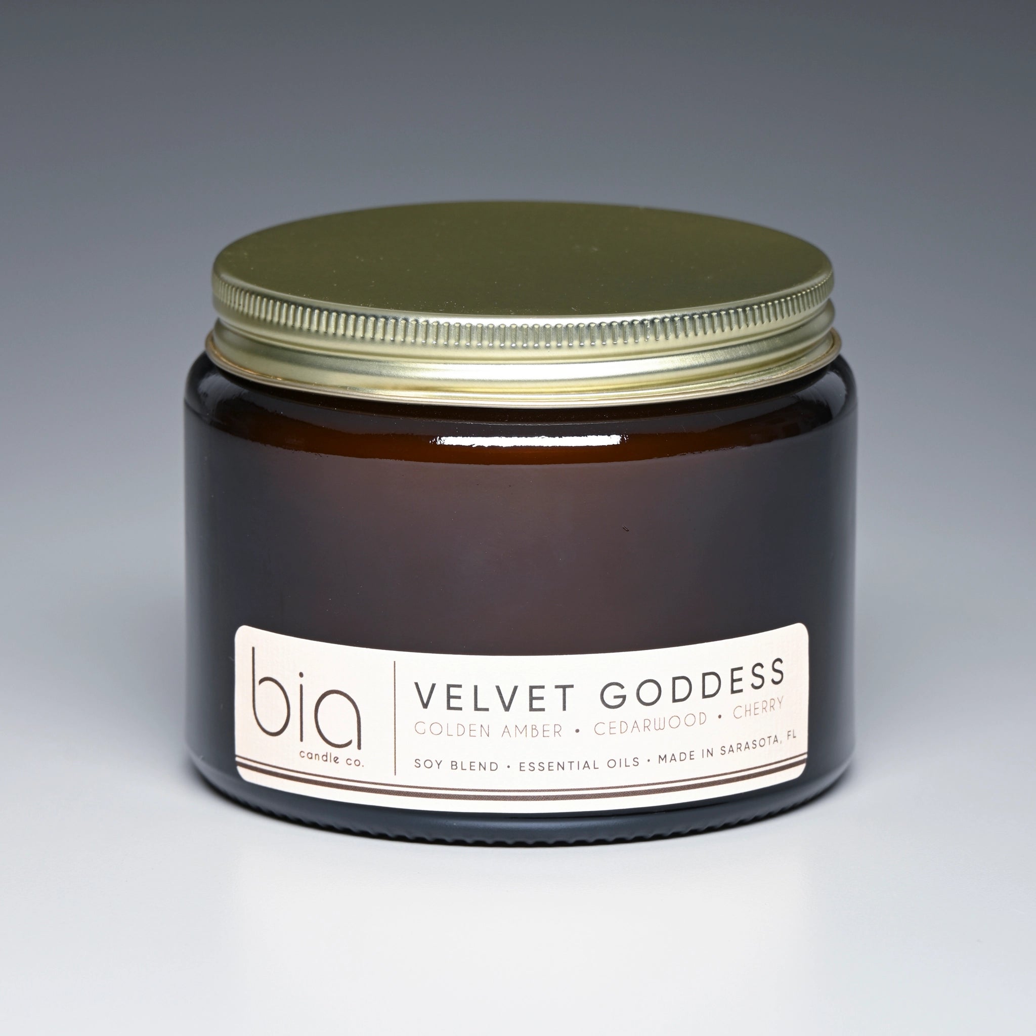 Jar of 'Velvet Goddess' candle by bia with a gold lid on a gradient background