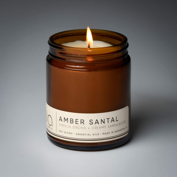 lit single wick amber santal soy candle on grey background
