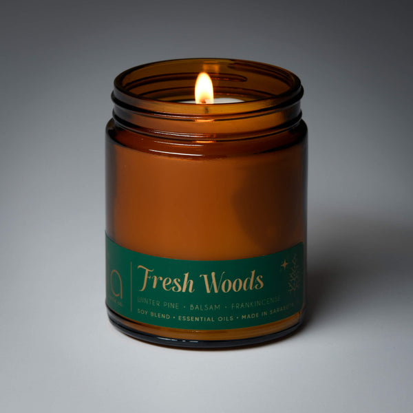 lit single wick holiday fresh woods soy candle on grey background