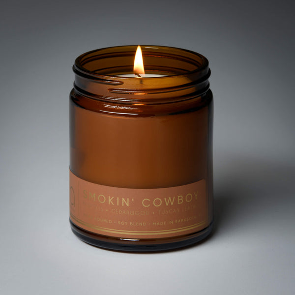 lit single wick smokin cowboy soy candle on grey background